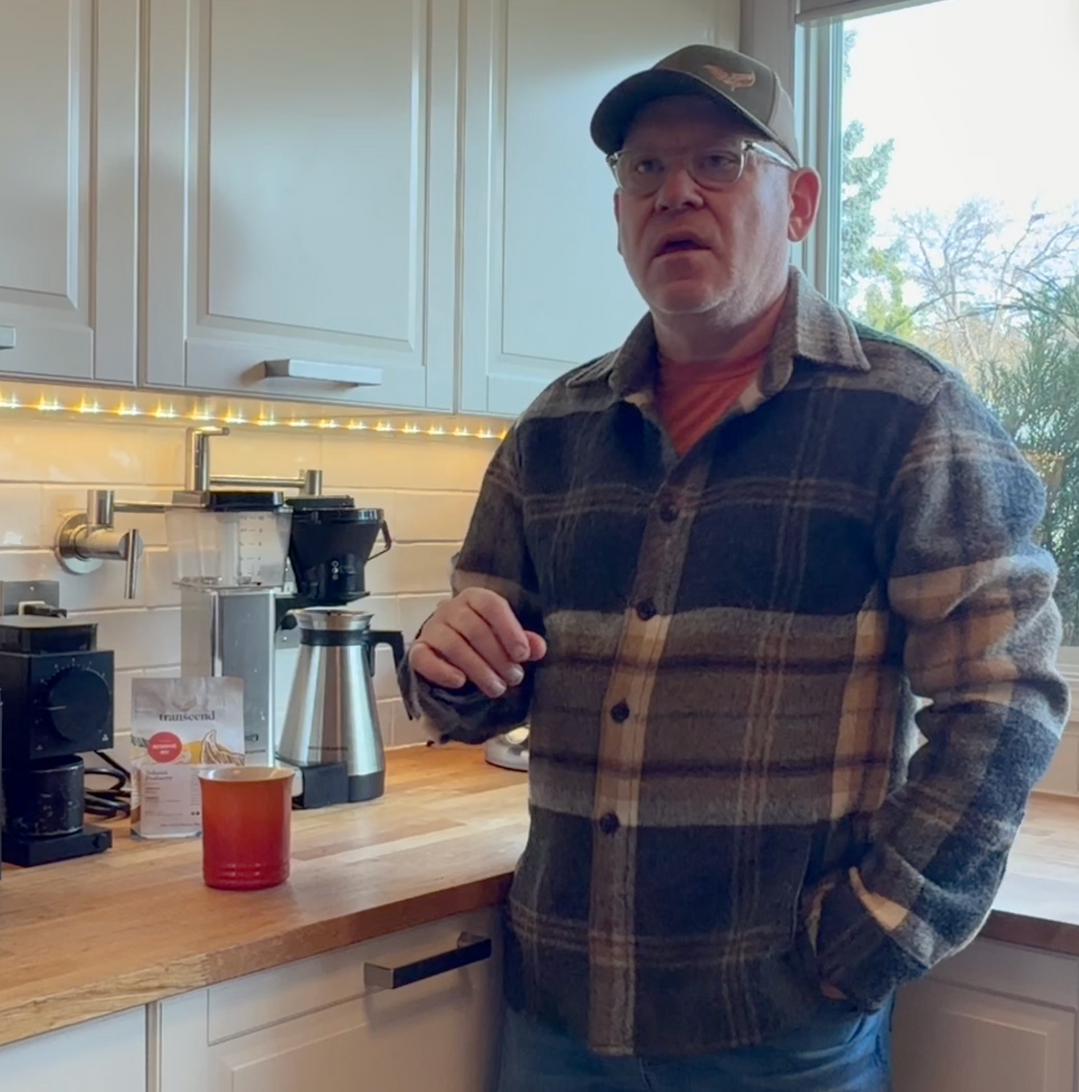 A picture of Poul Mark standing in his kitchen in front of a Moccamaster brewer, a Fellow Ode grinder and an orange Le Creuset coffee mug.